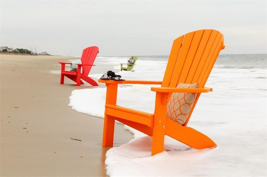 orange, red, and green Adirondack chairs sit in the ocean surf on a sandy beach