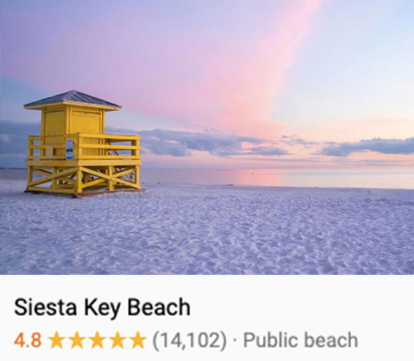 Photo of pink and purple clouds, light blue sky, and white sands taken from behind the yellow lifeguard tower at Siesta Key's public beach